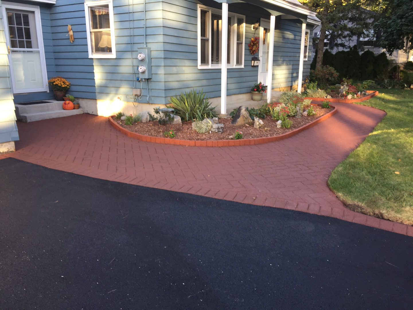Asphalt driveway with a red brick-pattern stamped asphalt border and walkway at a blue house.