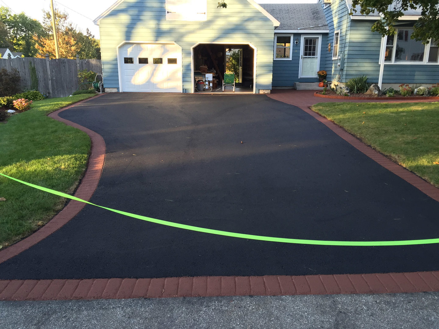 New asphalt driveway to a garage with a red brick-pattern stamped asphalt border.