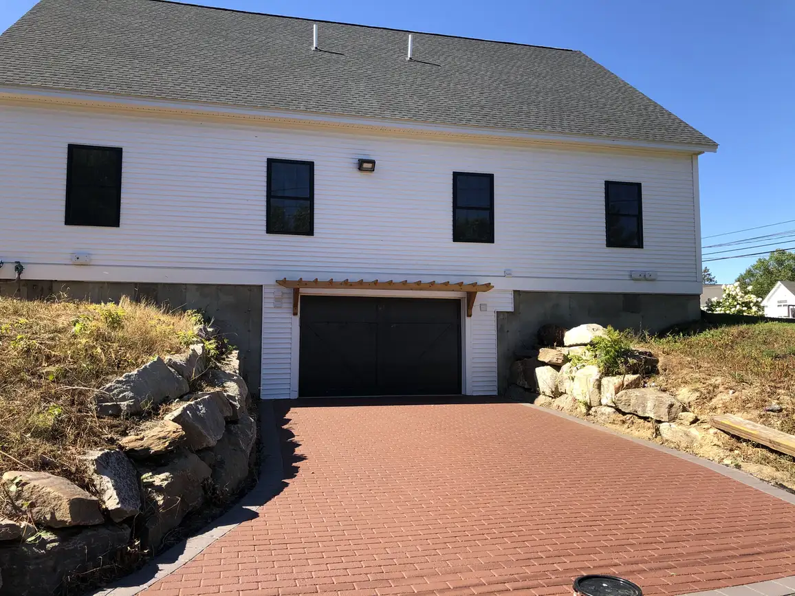 Red brick-pattern stamped asphalt driveway leading to a garage between stone retaining walls, Young's Excavating & Paving LLC, New Hampshire.