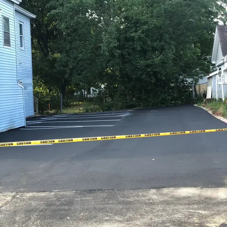 Freshly paved empty parking lot with yellow caution tape across the entrance and trees in the background.
