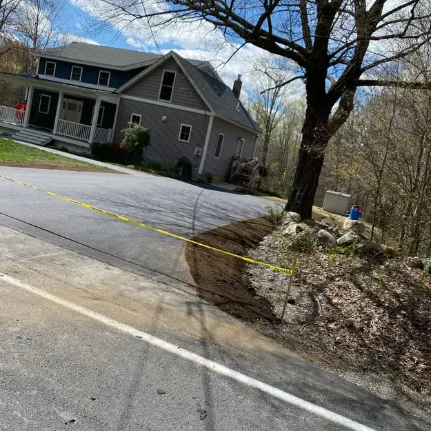 Two-story gray house on a residential street with a large bare tree and yellow caution tape marking a dirt area near the curb.