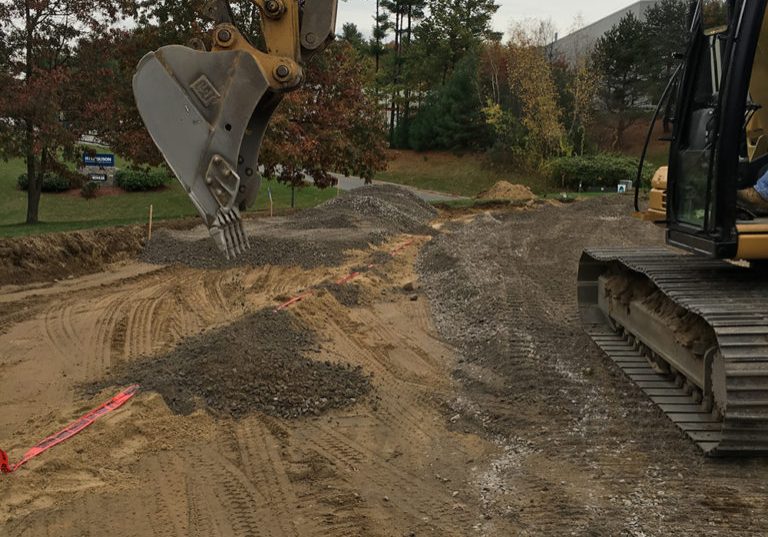 Excavator grading crushed stone during commercial site preparation.